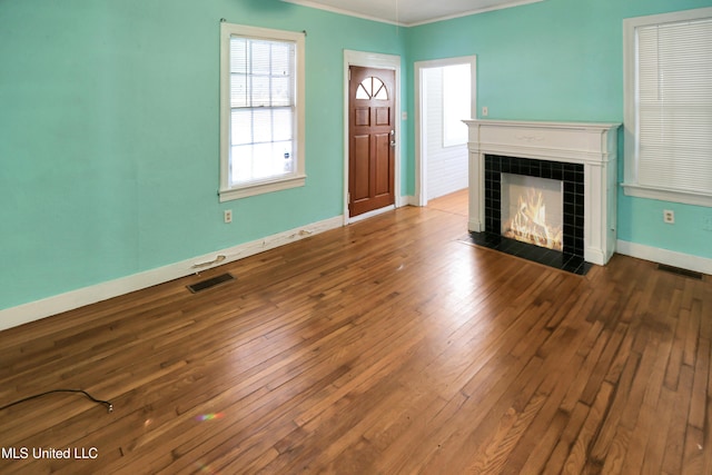 unfurnished living room featuring a tiled fireplace, crown molding, and hardwood / wood-style floors