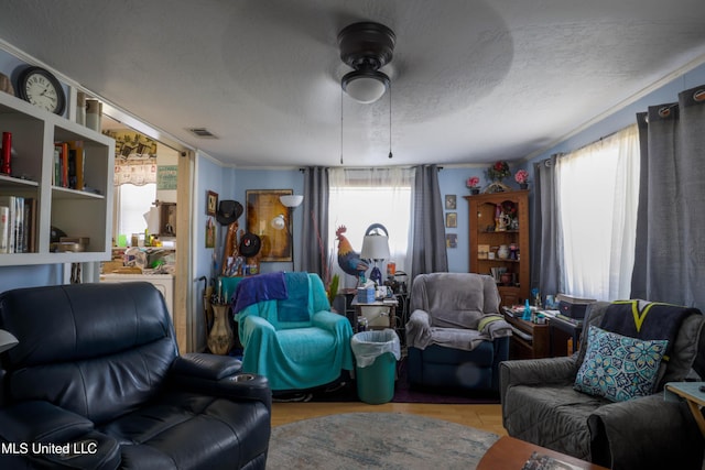 living room featuring a ceiling fan, visible vents, plenty of natural light, and a textured ceiling