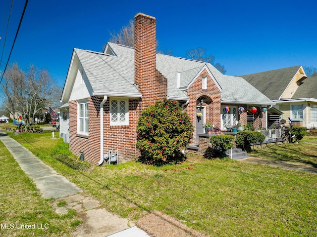 view of front of house featuring a shingled roof, a chimney, a front lawn, and brick siding