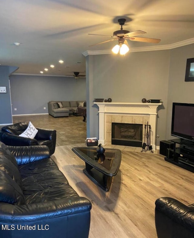 living room featuring ceiling fan, ornamental molding, wood-type flooring, and a tile fireplace