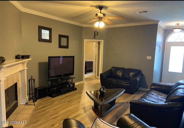 living room featuring a tiled fireplace, crown molding, light hardwood / wood-style flooring, and ceiling fan