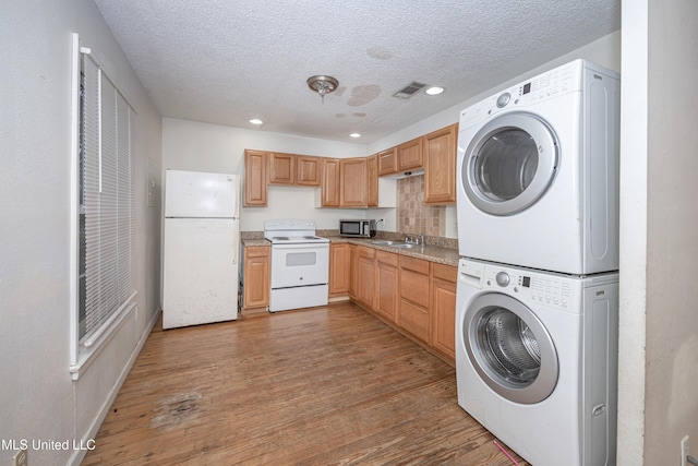 clothes washing area with hardwood / wood-style floors, stacked washer / drying machine, sink, and a textured ceiling