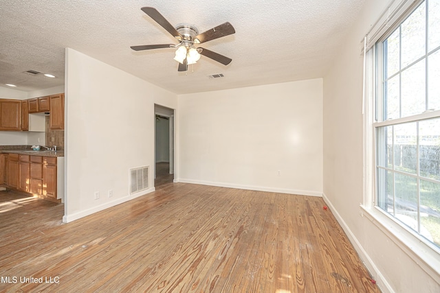 2411 12th St, Pascagoula, MS 39567 - unfurnished living room with light wood finished floors, a textured ceiling, plenty of natural light, and ceiling fan