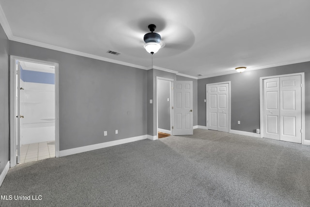 unfurnished bedroom featuring carpet, visible vents, two closets, and ornamental molding