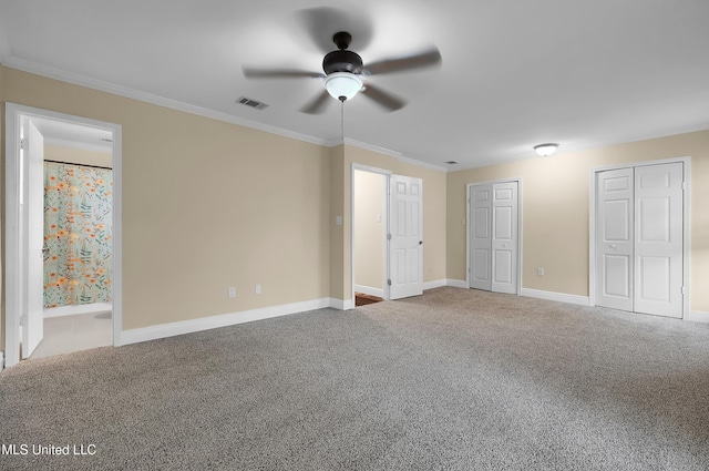 unfurnished bedroom with visible vents, baseboards, ornamental molding, carpet, and two closets