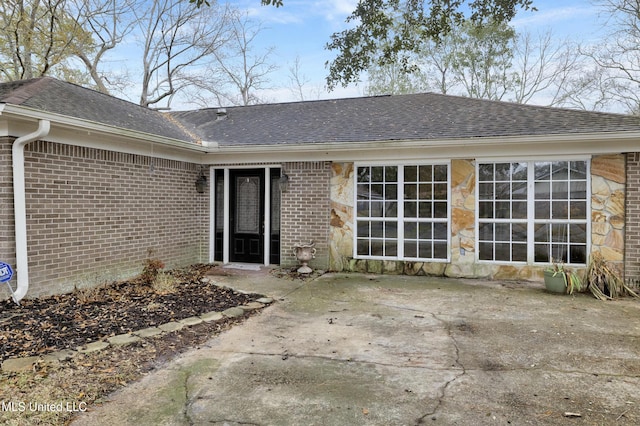 rear view of property featuring a shingled roof, a patio area, and brick siding