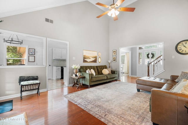 living room featuring a healthy amount of sunlight, high vaulted ceiling, ceiling fan with notable chandelier, and visible vents