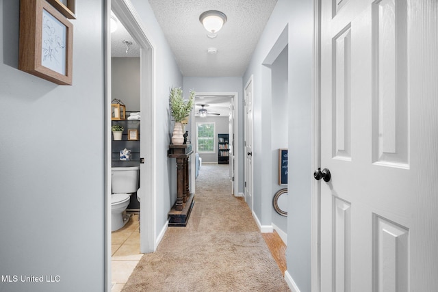 corridor featuring baseboards, a textured ceiling, and light colored carpet