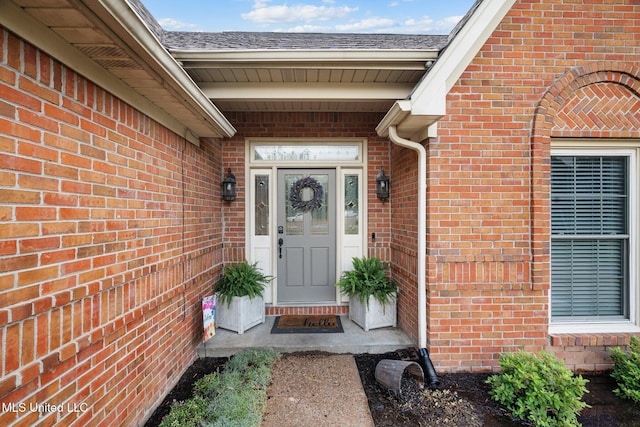 doorway to property featuring brick siding and a shingled roof