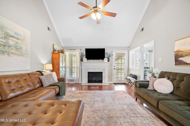 living room with a ceiling fan, visible vents, a fireplace with flush hearth, wood finished floors, and high vaulted ceiling