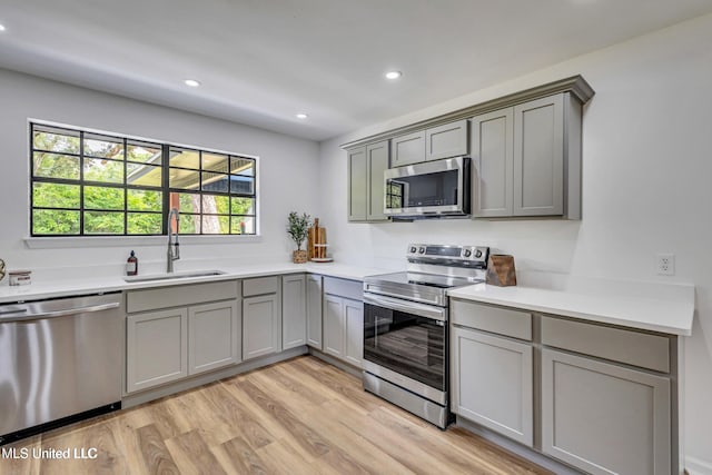 kitchen with gray cabinets, appliances with stainless steel finishes, sink, and light hardwood / wood-style flooring