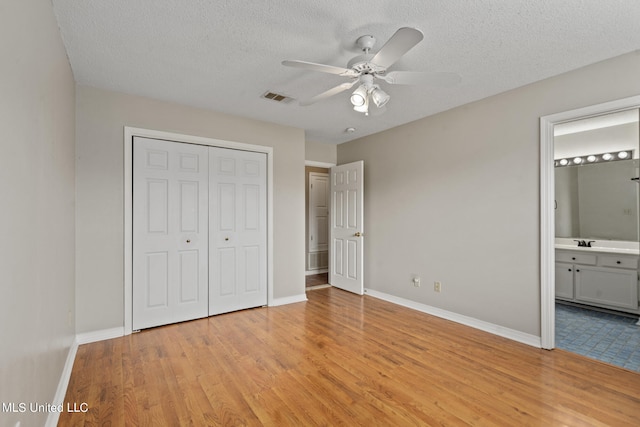 unfurnished bedroom with light wood-type flooring, a textured ceiling, a closet, ceiling fan, and connected bathroom