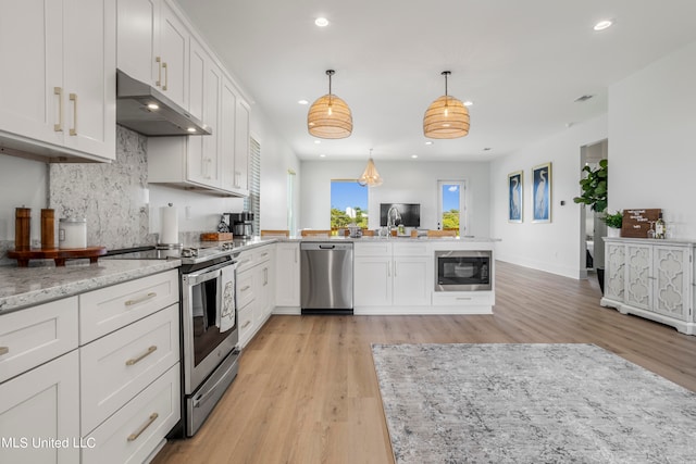 kitchen with stainless steel appliances, pendant lighting, white cabinets, light stone counters, and light hardwood / wood-style flooring