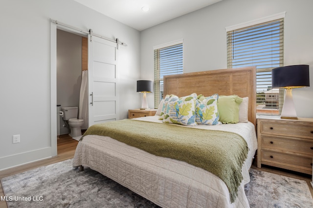 bedroom with multiple windows, hardwood / wood-style floors, a barn door, and connected bathroom