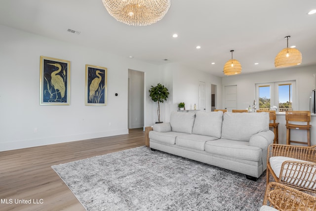 living room featuring light hardwood / wood-style flooring, french doors, and a notable chandelier