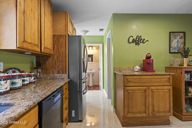 kitchen featuring stone countertops, visible vents, black dishwasher, brown cabinets, and stainless steel fridge