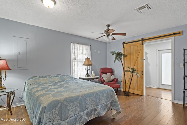 bedroom featuring visible vents, hardwood / wood-style floors, a barn door, a textured ceiling, and baseboards