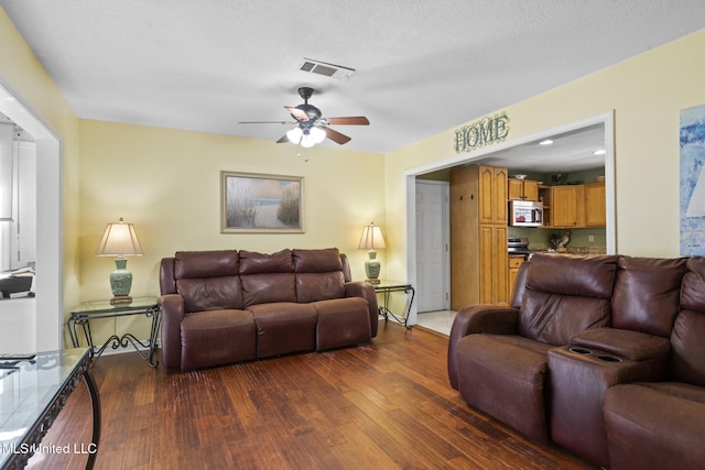 living area featuring a textured ceiling, dark wood-type flooring, visible vents, and a ceiling fan