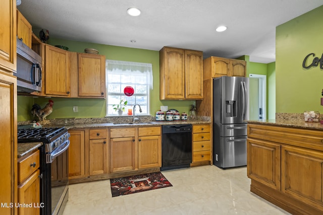 kitchen featuring stainless steel appliances, dark stone countertops, a sink, and brown cabinets