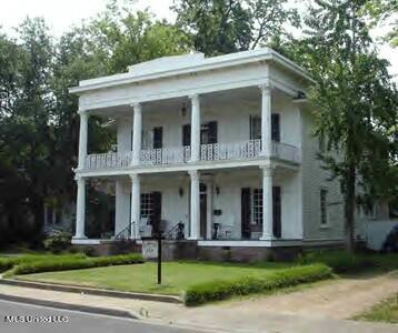 greek revival house featuring a front lawn and a balcony