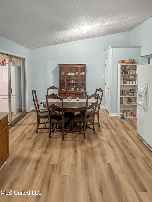 dining space featuring a textured ceiling, vaulted ceiling, and light hardwood / wood-style flooring