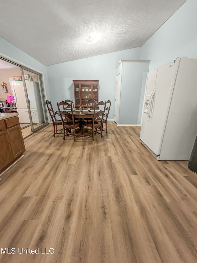 dining area with light hardwood / wood-style flooring, lofted ceiling, and a textured ceiling