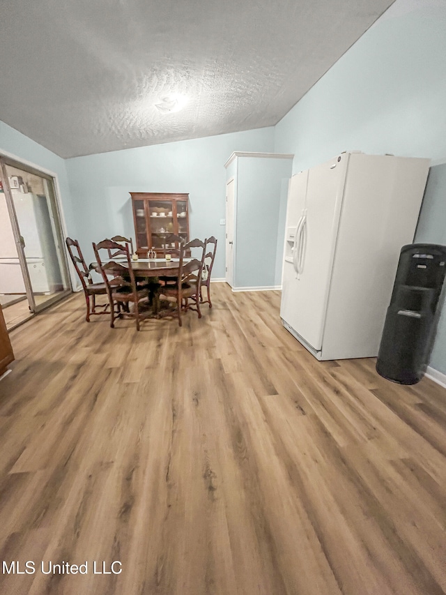 dining room with light hardwood / wood-style flooring, a textured ceiling, and vaulted ceiling