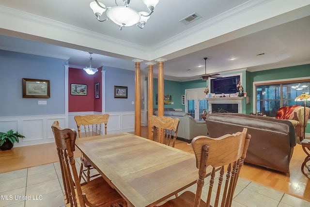 dining area with ceiling fan with notable chandelier, a wainscoted wall, light tile patterned floors, visible vents, and ornamental molding