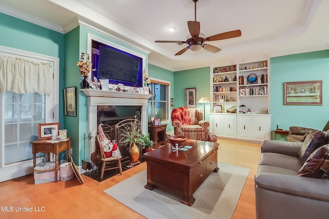 living room with built in features, crown molding, light wood-type flooring, and ceiling fan