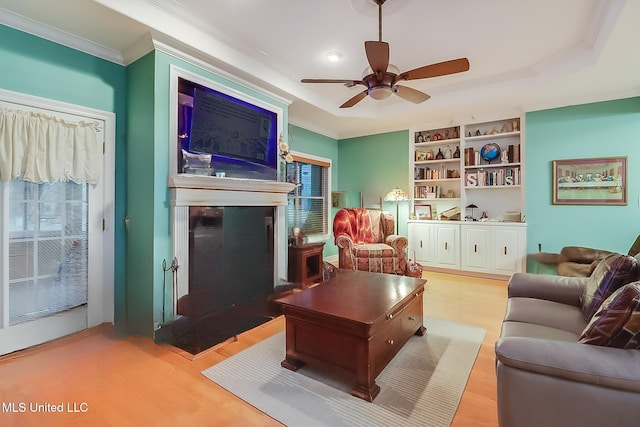 living room with crown molding, built in shelves, wood finished floors, and a fireplace
