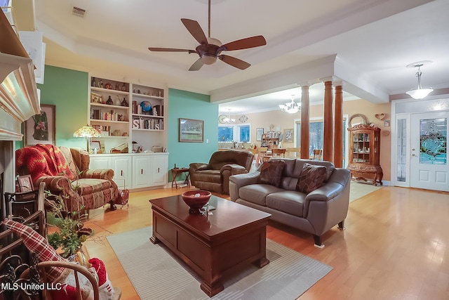 living room featuring decorative columns, visible vents, built in features, light wood-type flooring, and ceiling fan with notable chandelier