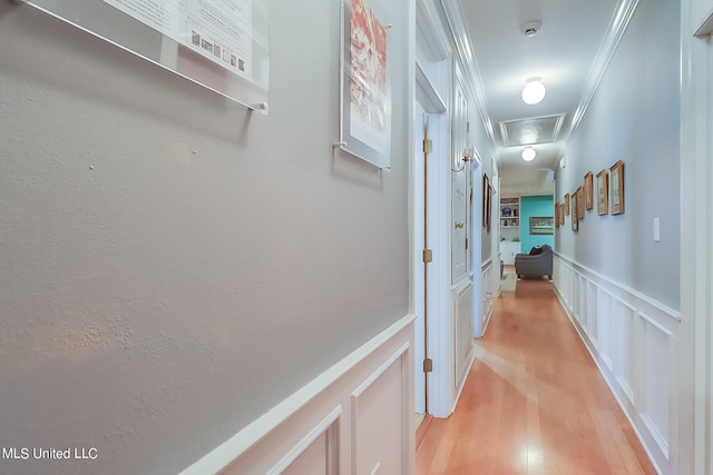 hall with attic access, crown molding, a wainscoted wall, a decorative wall, and light wood-style flooring