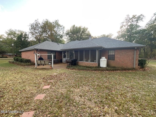 rear view of property featuring a lawn, a sunroom, and a patio area