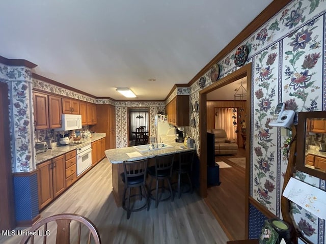 kitchen featuring white appliances, a kitchen breakfast bar, crown molding, light wood-type flooring, and kitchen peninsula