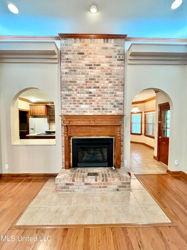 room details featuring white fridge with ice dispenser, crown molding, wood-type flooring, and a fireplace