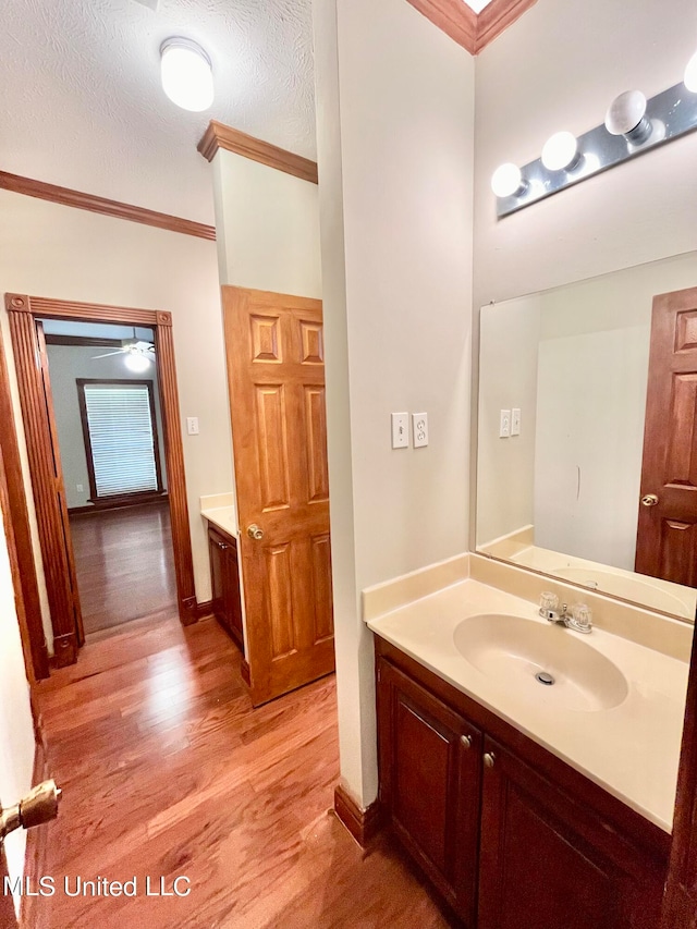 bathroom with hardwood / wood-style flooring, ornamental molding, vanity, a textured ceiling, and ceiling fan