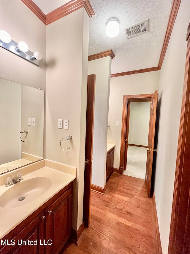 bathroom with vanity, crown molding, a textured ceiling, and hardwood / wood-style flooring