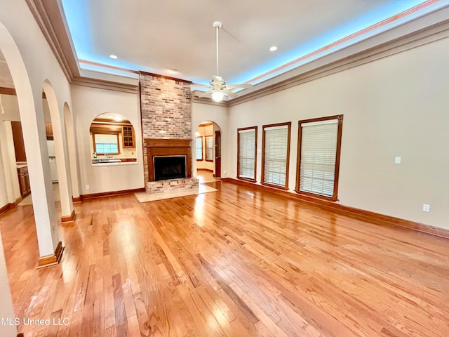 unfurnished living room featuring a brick fireplace, crown molding, light wood-type flooring, and ceiling fan