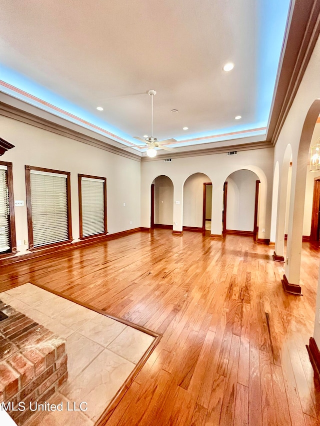 unfurnished living room with ornamental molding, a raised ceiling, light wood-type flooring, and ceiling fan