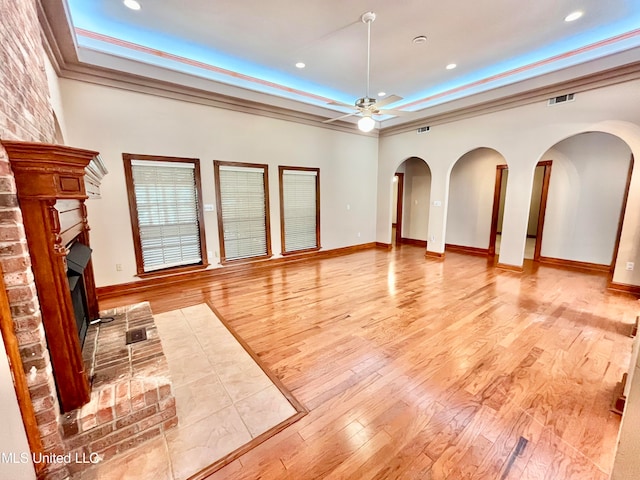 unfurnished living room with ceiling fan, ornamental molding, light wood-type flooring, and a fireplace