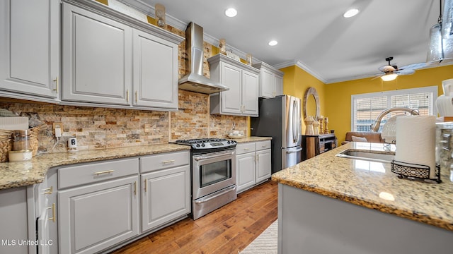 kitchen with wall chimney range hood, ceiling fan, light wood-type flooring, crown molding, and stainless steel appliances