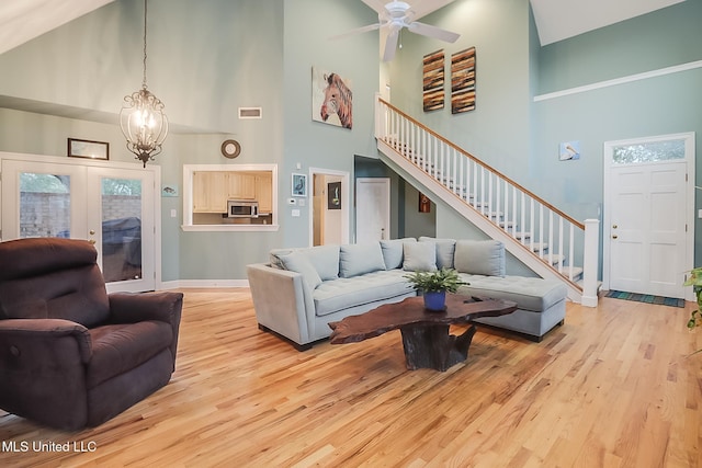 living room featuring ceiling fan with notable chandelier, french doors, high vaulted ceiling, and light hardwood / wood-style flooring