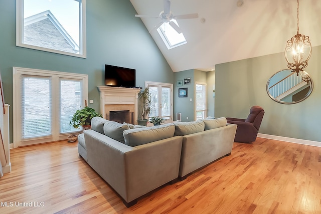 living room featuring ceiling fan with notable chandelier, a skylight, high vaulted ceiling, and light hardwood / wood-style flooring