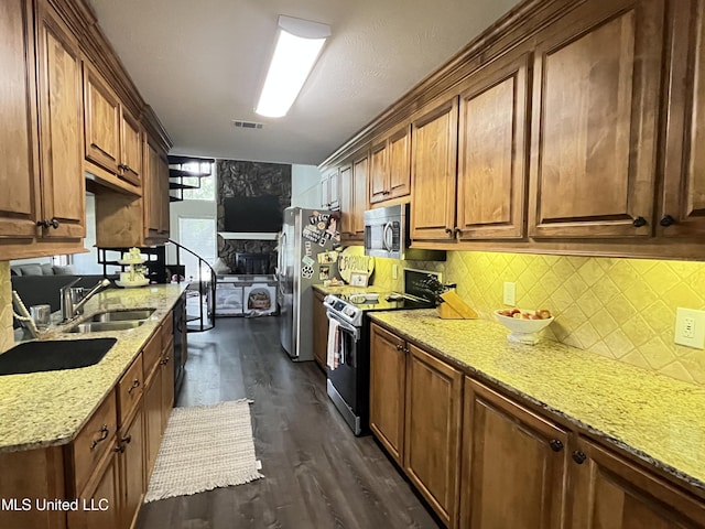 kitchen with sink, dark hardwood / wood-style flooring, stainless steel appliances, light stone counters, and decorative backsplash