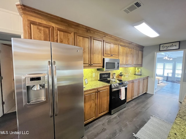 kitchen with dark hardwood / wood-style flooring, appliances with stainless steel finishes, light stone counters, and tasteful backsplash