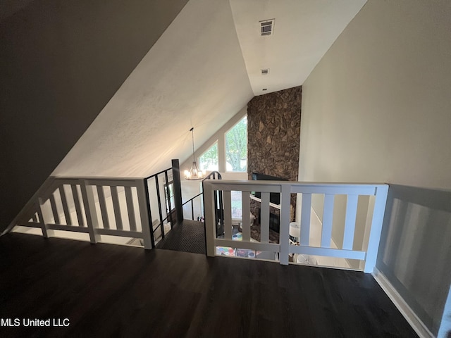 staircase featuring hardwood / wood-style flooring, lofted ceiling, a chandelier, and a stone fireplace