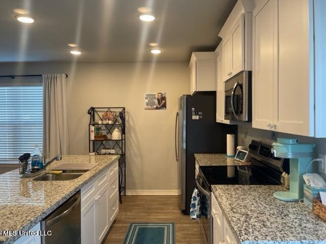 kitchen featuring appliances with stainless steel finishes, white cabinetry, light stone counters, and dark hardwood / wood-style flooring