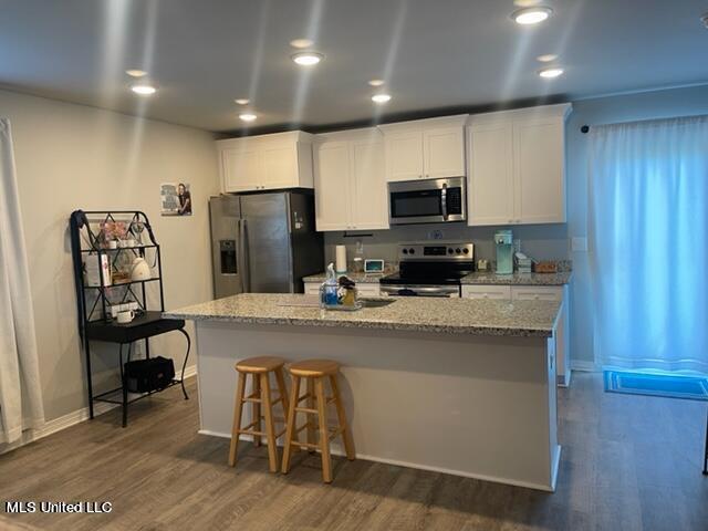 kitchen with white cabinets, a kitchen breakfast bar, stainless steel appliances, dark wood-type flooring, and a center island