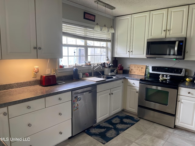 kitchen featuring stainless steel appliances, a sink, white cabinetry, dark countertops, and decorative light fixtures