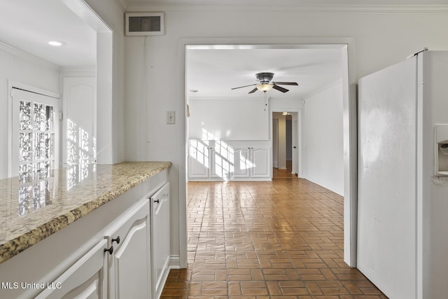 kitchen with white cabinetry, ceiling fan, light stone countertops, white refrigerator, and ornamental molding